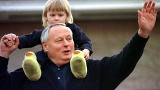 Als "Privatmann" winkt der zurückgetretene Bundesfinanzminister und SPD-Chef Oskar Lafontaine am Morgen des 13.3.1999 auf der Terrasse seines Hauses in Saarbrücken, auf den Schultern sein Sohn Carl-Maurice. "Macht schön Eure Fotos", ermuntert Lafontaine die wartenden Journalisten." Auf Fragen, warum er von allen politischen Ämtern zurückgetreten sei, sagt Lafontaine "Ich gebe keine Interviews." Er stehe hier als "Privatmann" und wolle jetzt bald spazierengehen. 