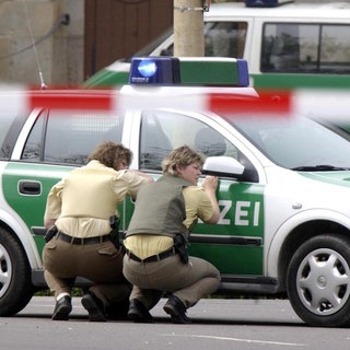 In Deckung gehen Polizeibeamtinnen hinter ihrem Wagen am Freitag, 26. April 2002 vor dem Gutenberg-Gymnasium in Erfurt. In einem  Amoklauf hat ein ehemaliger Schüler in diesem Gymnasium 17 Menschen und sich selbst erschossen. Mindestens vier Menschen wurden verletzt. 