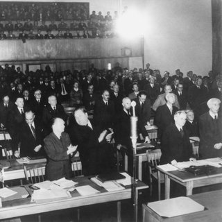 Gründung der Bundesrepublik Deutschland: Das Plenum des Parlamentarischen Rates nimmt in 3. Lesung am 8. Mai 1949 den revidierten Grundgesetzentwurf mit 53 gegen 12 Stimmen an. Vorne links: Max Reimann (sitzend), dahinter Heinz Renner, 3. von rechts: Carlo Schmid (stehend)