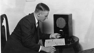 Radiohörer am 'Volksempfaenger' (hergestellt 1933 im Sachsenwerk). An der Wand Porträtaufnahmen von Adolf Hitler und Joseph Goebbels