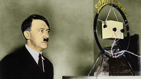 Adolf Hitler vor einem Radio-Mikrofon. Digital kolorierte Aufnahme aus dem Jahr 1933.