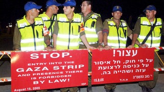 Iraelische Soldaten stehen am 15. August 2005 hinter einer Absperrung mit Schildern in Englisch und Hebräisch und blockieren die Straße in den Gazastreifen. Der Abzug Israels aus dem Gazastreifen ist im Gange. Viele Siedler verweigern die Kooperation.
