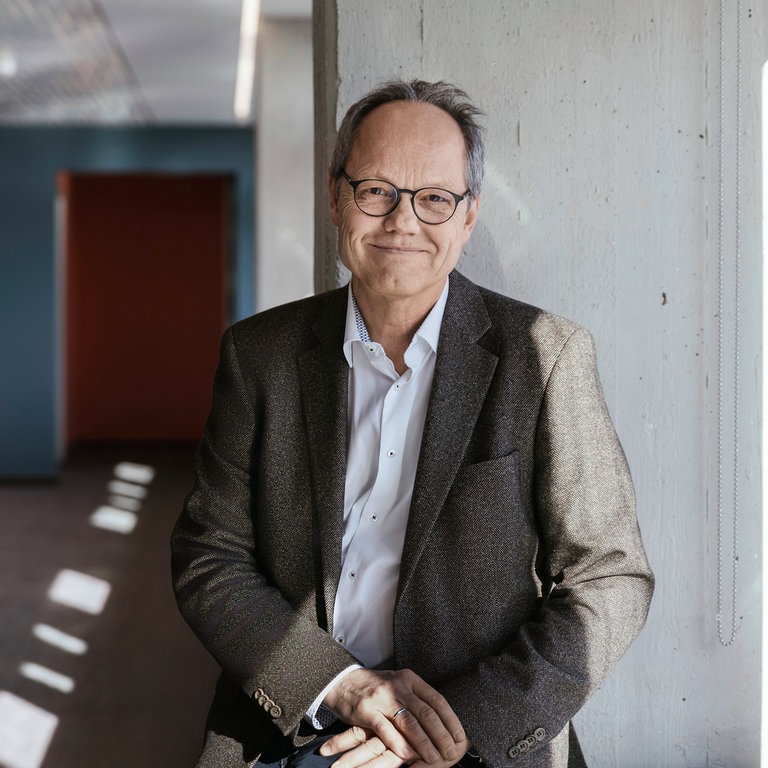 Der Intendant des SWR, Kai Gniffke, sitzt vor einer grauen Säule neben dem Fenster.