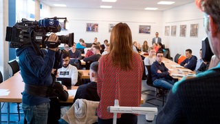 Redakteurin und Kameramann stehen vor Schulklasse