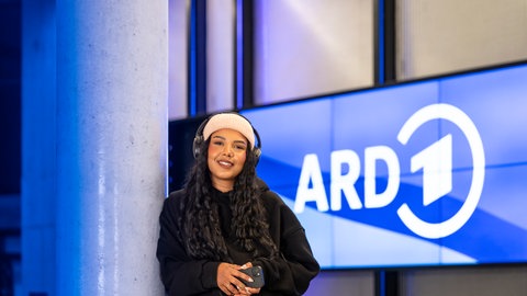 Kollegin vor der Monitorwand, auf der das ARD Logo zu sehen ist