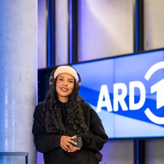 Kollegin vor der Monitorwand, auf der das ARD Logo zu sehen ist