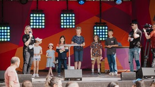 Kinder stehen auf der Bühne und raten bei dem Quiz von planet schule mit