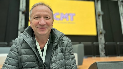 SWR Produktionsleiter Frieder Steiblmüller sitzt lächelnd vor einer Bühne 