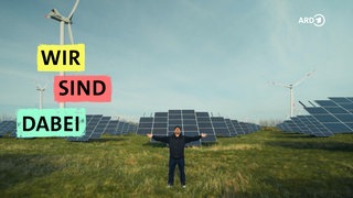 Bjarne Mädel steht mit ausgebreiteten Armen vor einem Solarpark