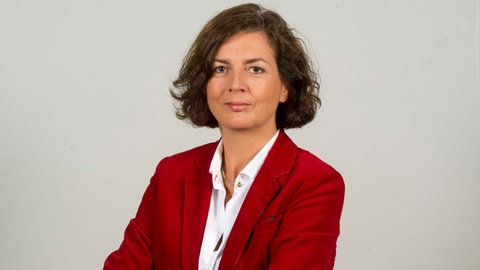 Sabine Oechsle trägt einen roten Blazer und verschränkt die Arme vor dem Körper