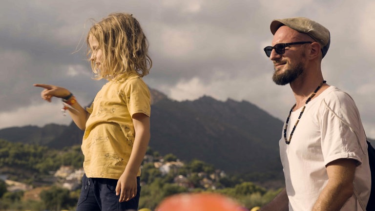 Phileas (links) und Max (rechts) schauen links aus dem Bild, im Hintergrund sind grüne Berge zu sehen.