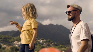 Phileas (links) und Max (rechts) schauen links aus dem Bild, im Hintergrund sind grüne Berge zu sehen.