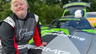 Angela im Rennanzug lehnt an einem Rennauto