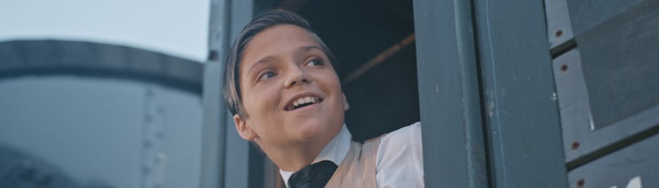 Thomas Alva Edison (Emile Cherif) beugt sich aus dem Fenster des fahrenden Zugs und lächelt.