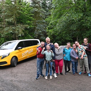 Die Reisegruppe steht vor ihrem Tourbus im Wald an der Geierlaybrücke