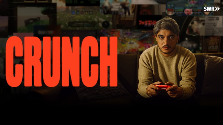"Crunch"-Keyvisual zeigt Host Khesrau Behroz mit Videospiel-Controller auf dem Sofa sitzend.