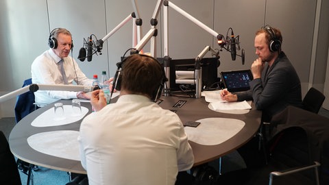 Christian Wulff (links) und die beiden SWR Hauptstadt-Korrespondenten Christopher Jähnert (rechts) und Kilian Pfeffer (Mitte) sitzen zusammen um einen Tisch im Studio