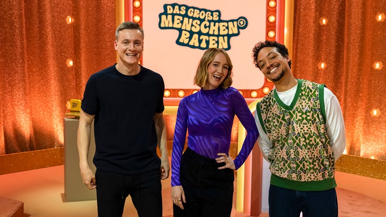 Aurel Mertz (rechts) mit seinen Gäst:innen Felix Kroos (links) und Mirella Precek (Mitte) in der modernen Spielshow im 70er-Jahre-Look.