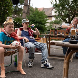 Christian (Camille Loup Moltzen), sein Bruder Benny (Len Blankenberg) und Opa Willy (André Eisermann) schauen Fernsehen