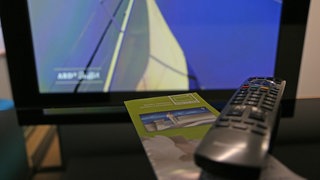 DVB-T2 HD Flyer vor Bildschirm mit Fernbedienung