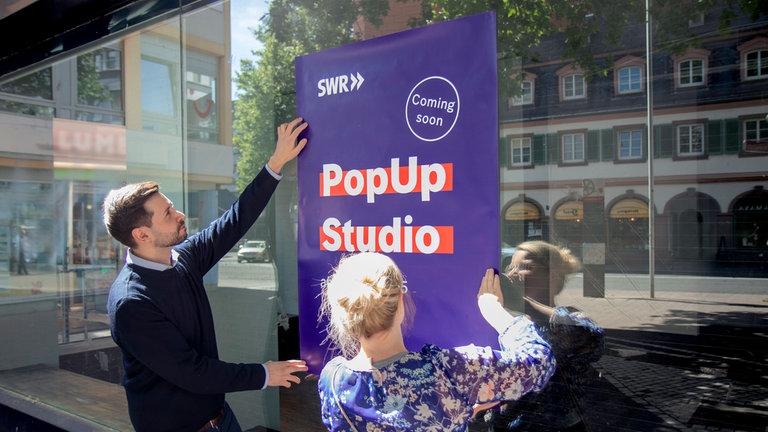 Annika Richter und Ibrahim Bilen vom SWR kleben Plakate am SWR PopUp Studio