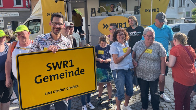Ein Mann hält ein Plakat mit der Aufschrift „SWR1 Heimspiel-Gemeinde“ in den Händen