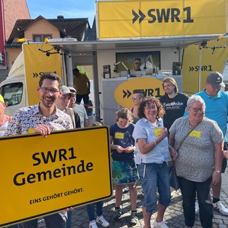 Ein Mann hält ein Plakat mit der Aufschrift „SWR1 Heimspiel-Gemeinde“ in den Händen