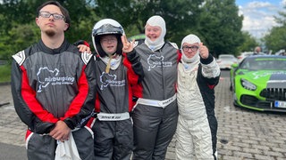Ein Teil der Gruppe steht in Vollmontur vor einem Rennauto am Nürburgring (v.l.n.r. Jonas, Rosalie, Angela, Patrick)