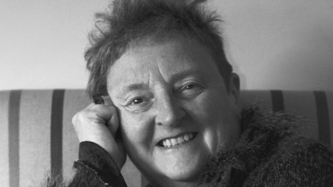 Leona Jones sitz auf einer Couch und lächelt in die Kamera