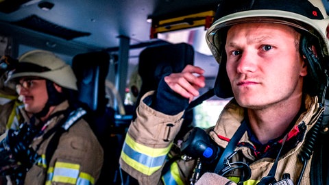 Zwei Feuerwehrmänner in Montur im Einsatzfahrzeug