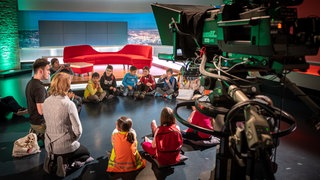 Kinder in einem Sitzkreis auf dem Boden eines Fersehstudios