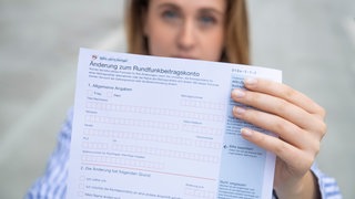 Das bild zeigt eine Frau, die ein Formular zum Rundfunkbeitrag in der Hand hält