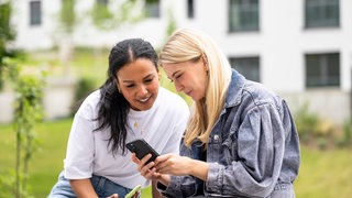 kolleginnen-schauen-auf-smartphone-draußen