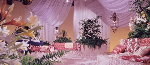 Bühnenbild zur Sendung: Gute Laune mit Musik. Rosa Flokati liegt auf der Bühne verteilt. Rote Samtkissen zieren die Sitzecken, Chiffontücher schmücken wellenartig die Studiodecke. Vereinzelte Blumenarrangements sind zwischen den Sitzecken platziert.