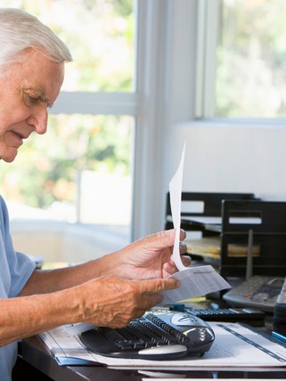 Alter Mann blickt auf einen Zettel, Schreibtisch, Rente, Frührente, Hinzuverdienst, Rentner