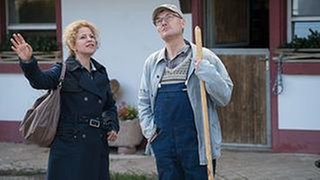 Bea und Karl vor dem Fallerhof, Bea macht eine ausschweifende Geste Richtung Himmel