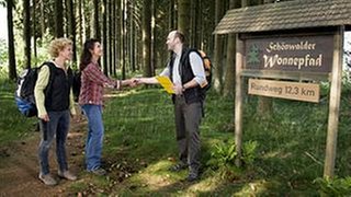 Bea und Monique begrüßen den Prüfer vor dem Schild zum Wonnepfad