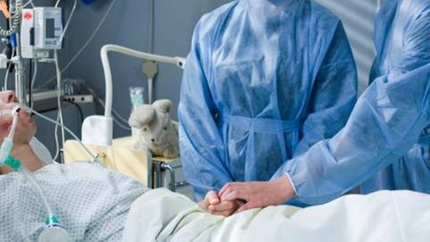 Jenny und Celine stehen bei Albert, der im Koma liegt, am Krankenbett