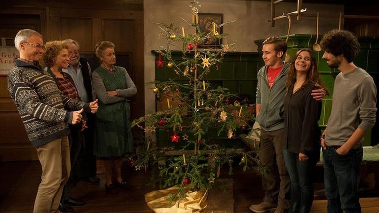 Die Familie ist im Wohnzimmervor dem Kachelofen um den Christbaum versammelt
