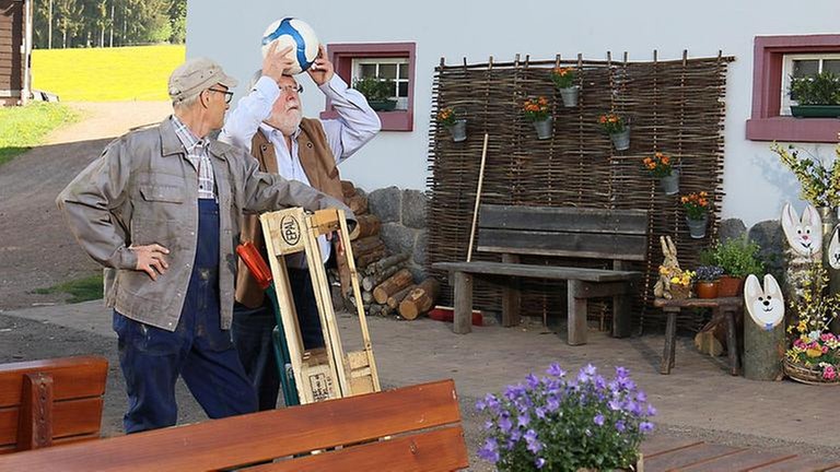 Hermann versucht, einen Fußball auf dem Kopf zu balancieren, Karl steht neben ihm