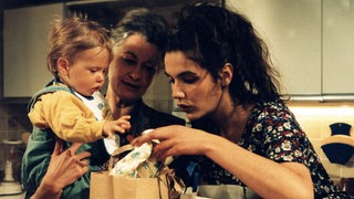 Johanna, Baby Albert und Monique vor Einkauftaschen, die auf dem Tisch stehen