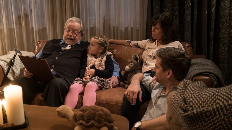 Hermann liest Carlotta eine Geschichte vor, Eva und Andreas sitzen dabei und lauschen