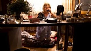 Frau Heilert kniet im Nachthemd vor ihrem Schreibtisch und telefoniert