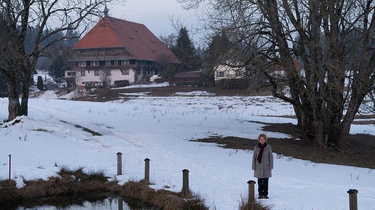 Bea steht auf schneebedeckter Wiese am Weiher, im Hintergrund der Fallerhof