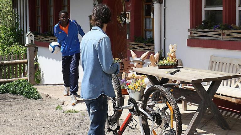 Albert repariert sein Fahrrad, Tayo kommt mit einem Fußball unterm Arm aus dem Haus
