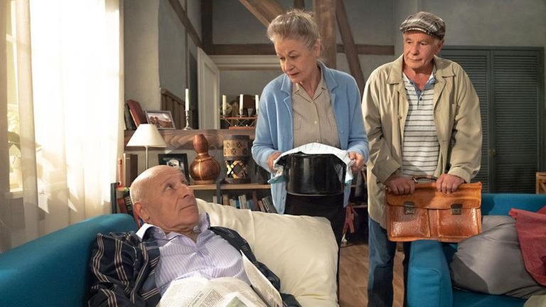 Johanna und Heinz kümmern sich um den krank auf dem Sofa liegenden Franz