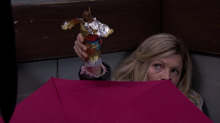 Frau Heilert versteckt sich hinter einem rosa Regenschirm und hält einen Schokoladenosterhasen hoch