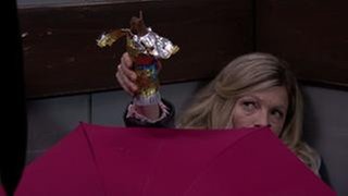 Frau Heilert versteckt sich hinter einem rosa Regenschirm und hält einen Schokoladenosterhasen hoch