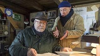 Hermann sitzt am Schreibtisch im Sägewerksbüro, Toni redet auf ihn ein