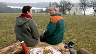 Rosi und Karl sitzen nach getaner Arbeit auf einem Baumstamm und machen Pause